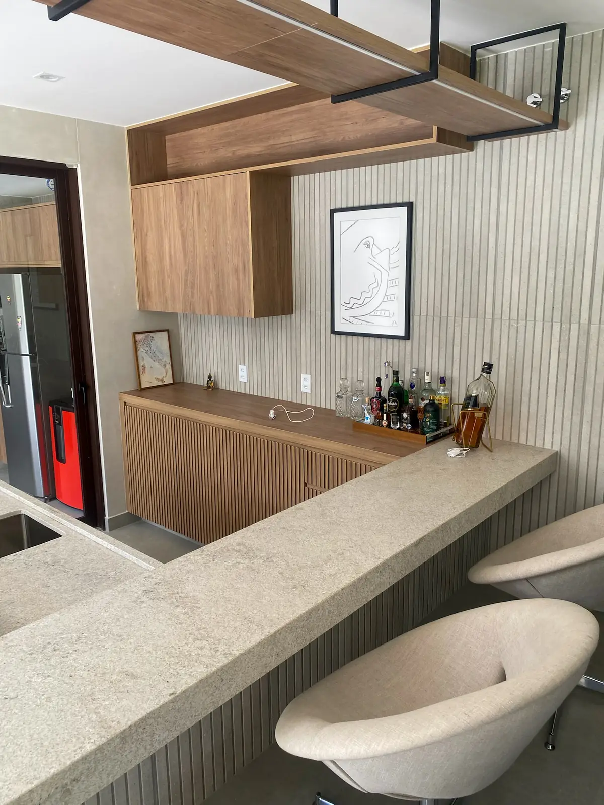 Bar planejado em madeira ripada com nicho para garrafas, bancada em granito e banquetas