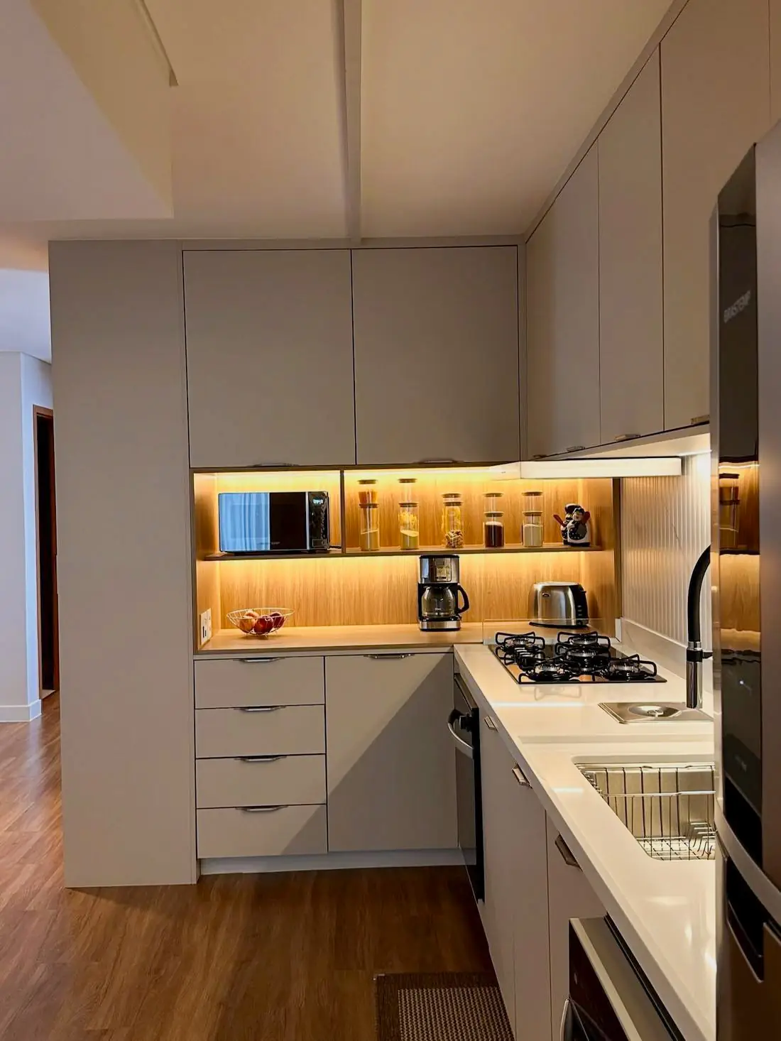 Nicho de cozinha iluminado com cafeteira, torradeira e potes organizados