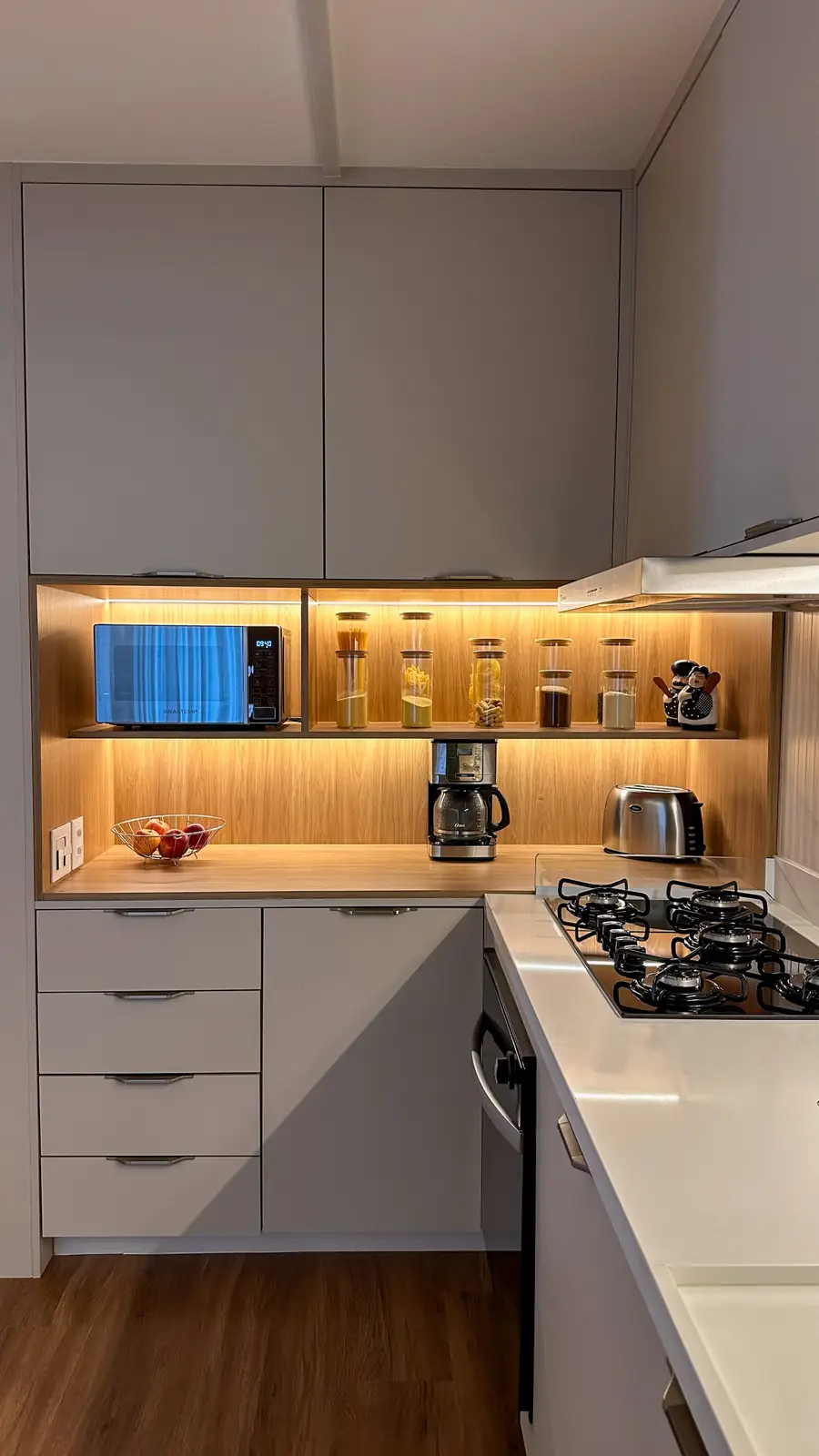 Cozinha compacta cinza com nicho iluminado para cafeteira e potes organizadores